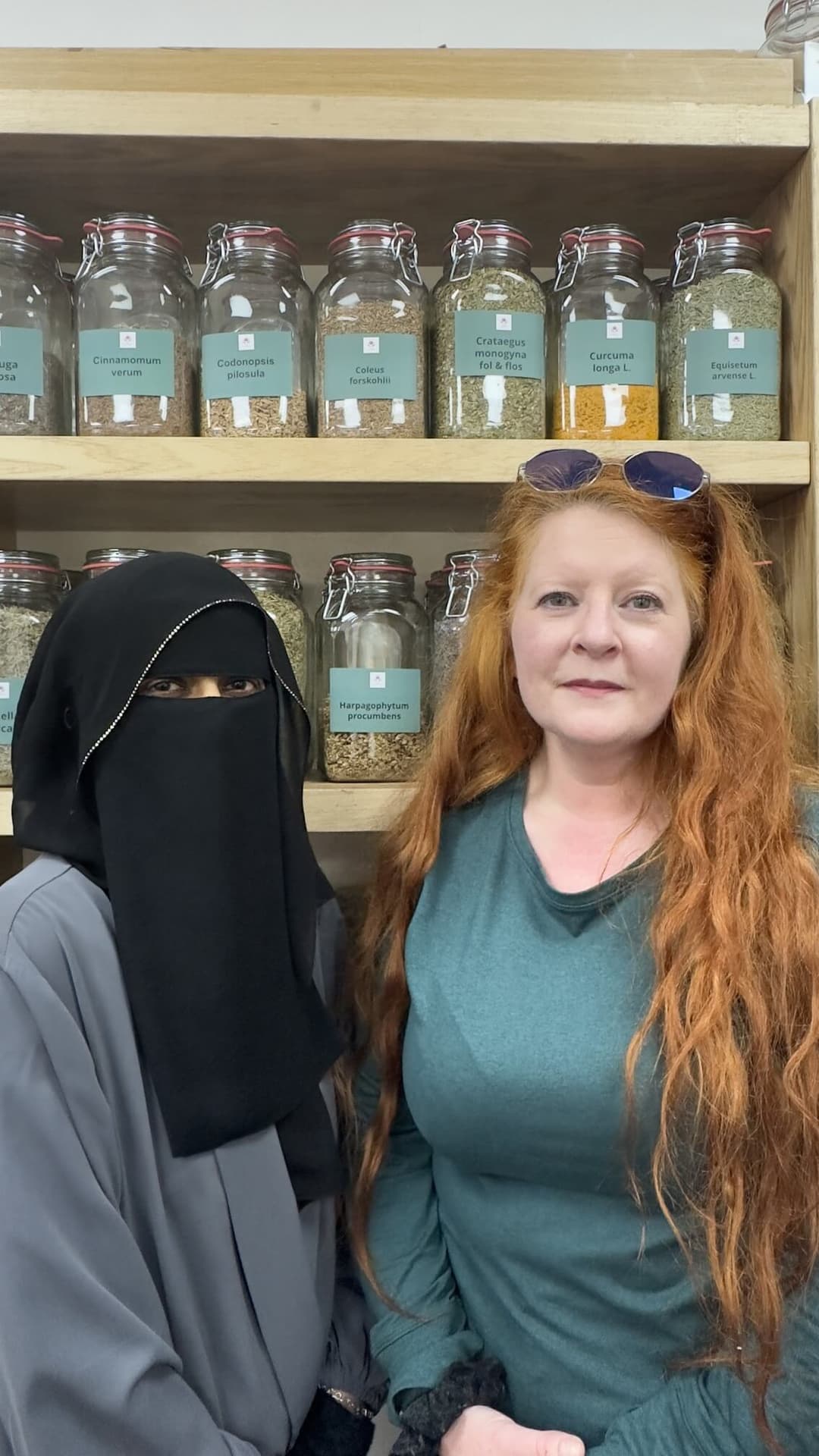 The two practitioners of The Essence of Woman in front of shelves of dried herbs in labelled jars